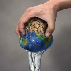 Mano che stringe la Terra, con terra arida che si sgretola e acqua che cola. Simboleggia il significato di overshoot day: il giorno in cui consumiamo più risorse di quelle che il pianeta può rigenerare.
