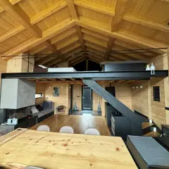 Interno di una baita con splendidi tetti in legno a vista, camino moderno, soppalco e arredi accoglienti.