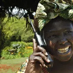 Wangari Muta Maathai sorride mentre parla al telefono, con uno sfondo verdeggiante.
