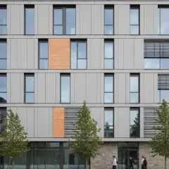 Facciate ventilate prezzi: edificio moderno con pannelli grigi e arancioni, finestre ampie e alberi.