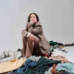 Donna pensierosa seduta su un cumulo di vestiti, simbolo del consumismo del brand fast fashion.