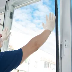 Operaio con guanti bianchi effettua la sostituzione vetro finestra, con cielo azzurro e nuvole sullo sfondo.