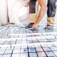 Installazione di tubi per il raffrescamento a pavimento. Un operaio srotola un grosso rotolo di tubo bianco su una griglia isolante.