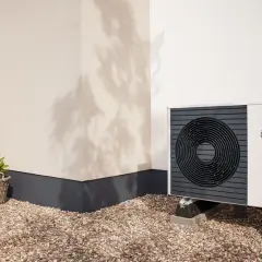 Pompa di calore climatizzatore Vaillant aroTHERM plus, un'unità esterna moderna su un patio ghiaioso, con un piccolo ulivo e un cesto di fiori.