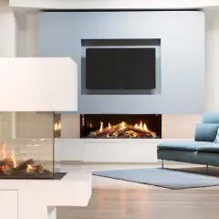 Modern living room with two elegant caminetti senza canna fumaria, one with glass enclosure, and a TV above a fireplace.