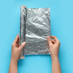 Mani che srotolano la pellicola dove si butta, un rotolo di alluminio su sfondo blu.