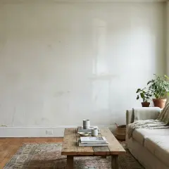 Soggiorno con divano beige, tavolino in legno e pareti che mostrano le imperfezioni, suggerendo tecniche di pittura pareti per un look rustico.