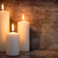 Tre candele di cera bianca illuminate, con fiamme danzanti, su uno sfondo scuro. Un'atmosfera intima, perfetta per riflettere su dove si buttano le candele di cera.