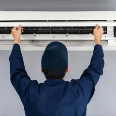 Tecnico apre il pannello di un condizionatore split per manutenzione. Il riscaldamento con split è efficiente.