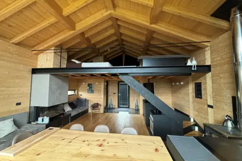 Interno di una baita con splendidi tetti in legno a vista, camino moderno, soppalco e arredi accoglienti.