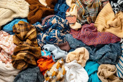 Un mucchio di vestiti colorati, pronti per la raccolta indumenti usati. Maglioni, sciarpe e tessuti di varie fantasie e trame.
