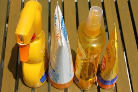 Prodotti solari scaduti, tra cui una crema solare spray e una lozione, pronti per essere smaltiti. Dove si buttano le creme scadute?