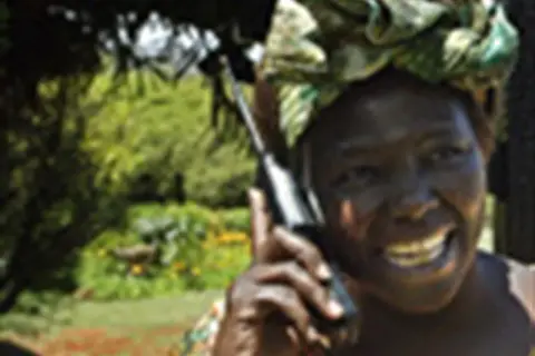 Wangari Muta Maathai sorride mentre parla al telefono, con uno sfondo verdeggiante.