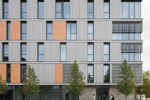 Facciate ventilate prezzi: edificio moderno con pannelli grigi e arancioni, finestre ampie e alberi.