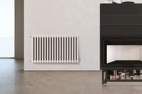 Termocamino moderno con dettagli idraulici visibili sotto, accanto a un radiatore bianco. Illustra come funziona un termocamino per riscaldare l'ambiente.