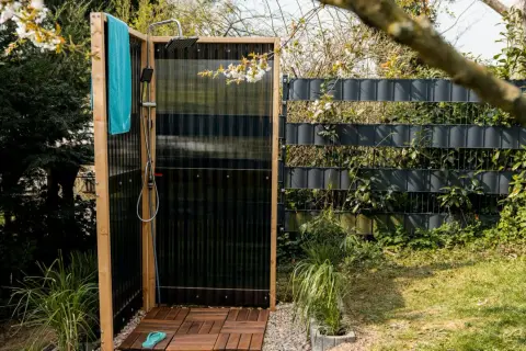 Doccia da giardino fai da te con pedana in legno, telo azzurro e rubinetto. Perfetta per rinfrescarsi all'aperto.