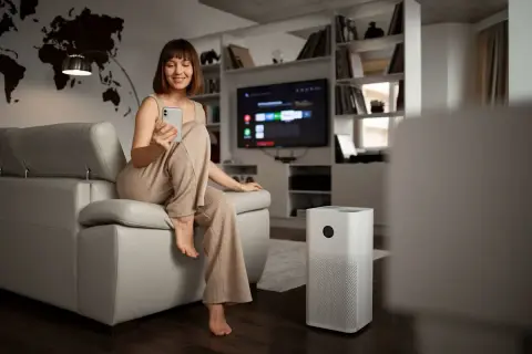 Donna sorride usando il telefono accanto a un deumidificatore. Questo dispositivo aiuta a mantenere l'aria sana.