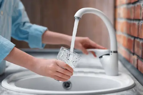 Mani che riempiono un bicchiere d'acqua dal rubinetto. L'acqua sanitaria cos'è? È l'acqua potabile che arriva nelle nostre case.