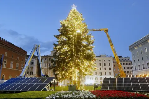 Un imponente albero di Natale illuminato, circondato da pannelli solari, simboleggia un futuro più verde per le festività.