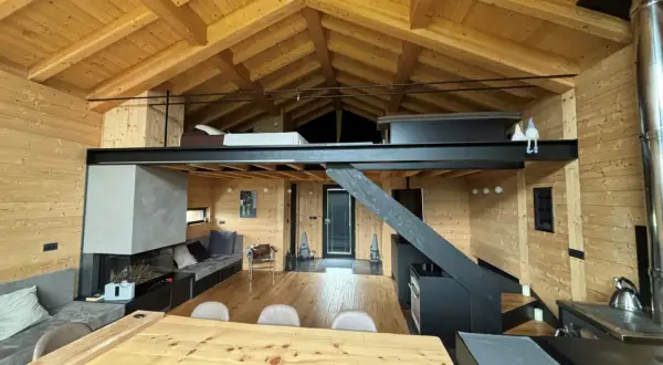 Interno di una baita con splendidi tetti in legno a vista, camino moderno, soppalco e arredi accoglienti.