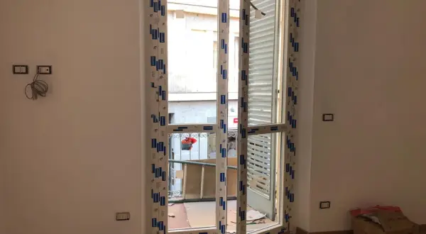 Nuova **doppia finestra per isolamento termico** installata in un ambiente in fase di ristrutturazione. Si intravede un cortile esterno.