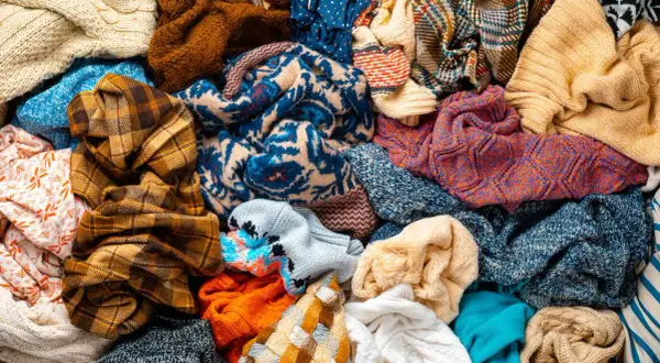 Un mucchio di vestiti colorati, pronti per la raccolta indumenti usati. Maglioni, sciarpe e tessuti di varie fantasie e trame.
