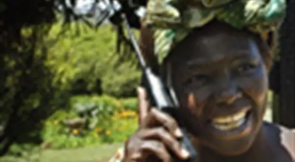 Wangari Muta Maathai sorride mentre parla al telefono, con uno sfondo verdeggiante.