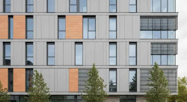 Facciate ventilate prezzi: edificio moderno con pannelli grigi e arancioni, finestre ampie e alberi.