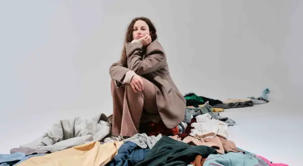 Donna pensierosa seduta su un cumulo di vestiti, simbolo del consumismo del brand fast fashion.