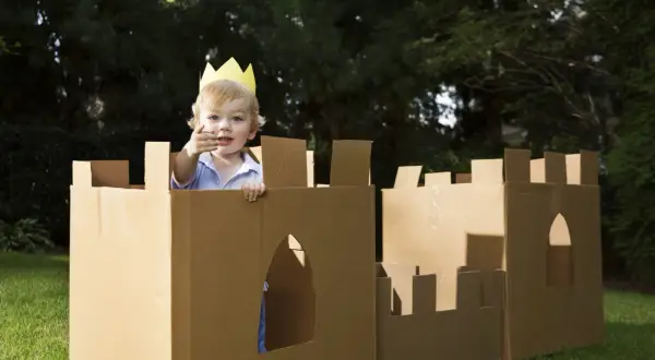 Bambino con corona gioca in un castello fatto con giochi fai da te con cartone, in giardino.