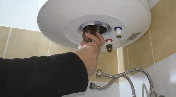 Mano che estrae la resistenza scaldabagno elettrico. Riparazione fai da te.