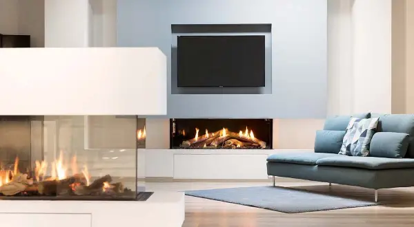 Modern living room with two elegant caminetti senza canna fumaria, one with glass enclosure, and a TV above a fireplace.