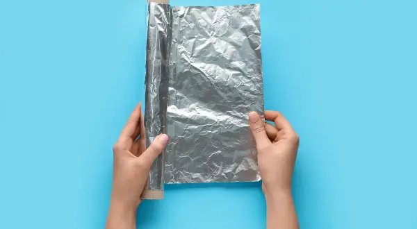 Mani che srotolano la pellicola dove si butta, un rotolo di alluminio su sfondo blu.