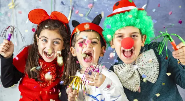 Bambini festosi con vestiti di carnevale creativi, realizzati con materiale riciclato, lanciano coriandoli.