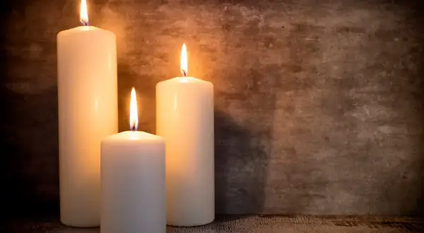 Tre candele di cera bianca illuminate, con fiamme danzanti, su uno sfondo scuro. Un'atmosfera intima, perfetta per riflettere su dove si buttano le candele di cera.