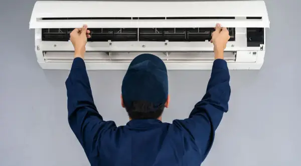 Tecnico apre il pannello di un condizionatore split per manutenzione. Il riscaldamento con split è efficiente.