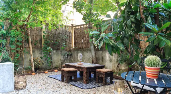 Un angolo zen per il tuo progetto giardino 50 mq: tavolino intagliato, sgabelli, Buddha e cactus.