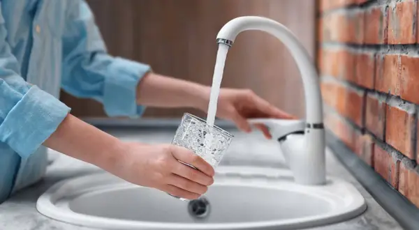 Mani che riempiono un bicchiere d'acqua dal rubinetto. L'acqua sanitaria cos'è? È l'acqua potabile che arriva nelle nostre case.