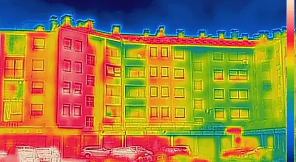 Analisi termica di un edificio con termocamera per edilizia: zone rosse indicano dispersioni di calore, verdi e blu zone più fredde.