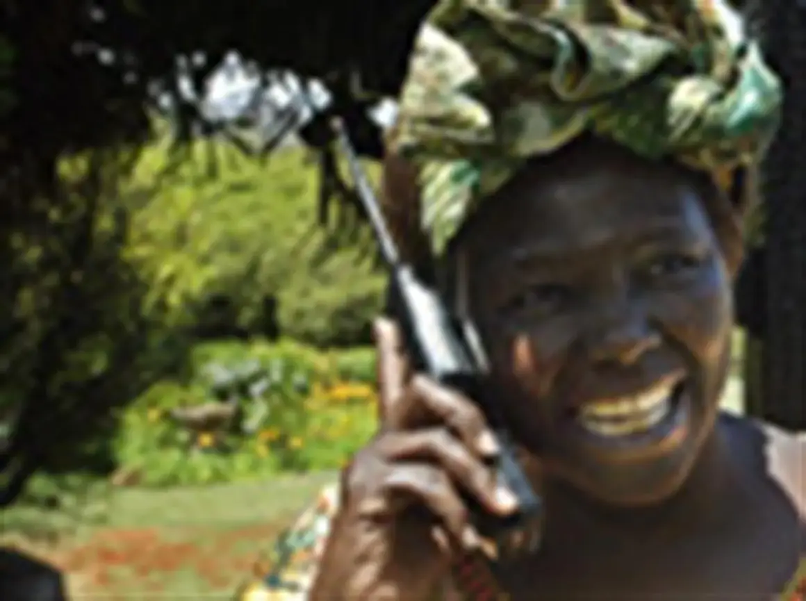 Wangari Muta Maathai sorride mentre parla al telefono, con uno sfondo verdeggiante.