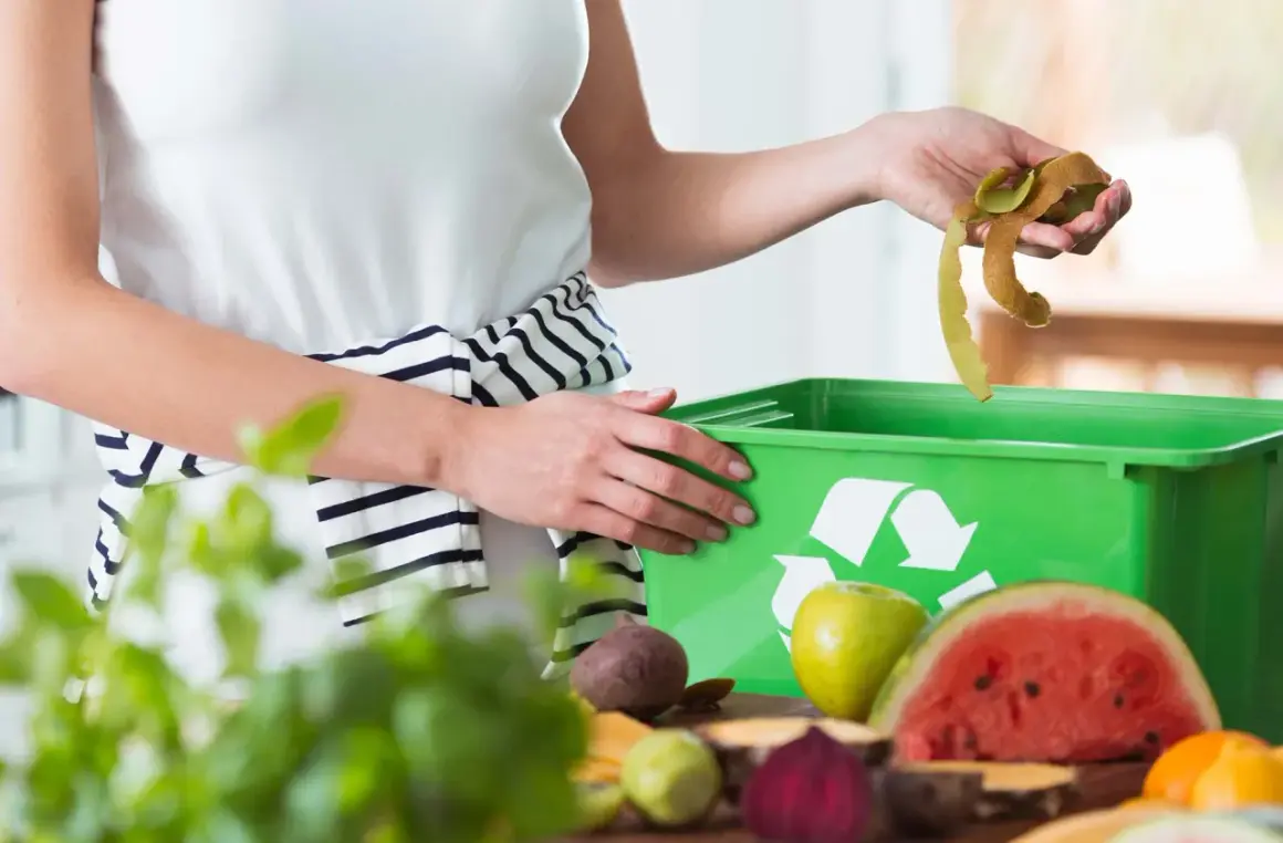 Mani che gettano bucce di frutta in un contenitore verde per ridurre i rifiuti. Frutta e verdura sul tavolo.