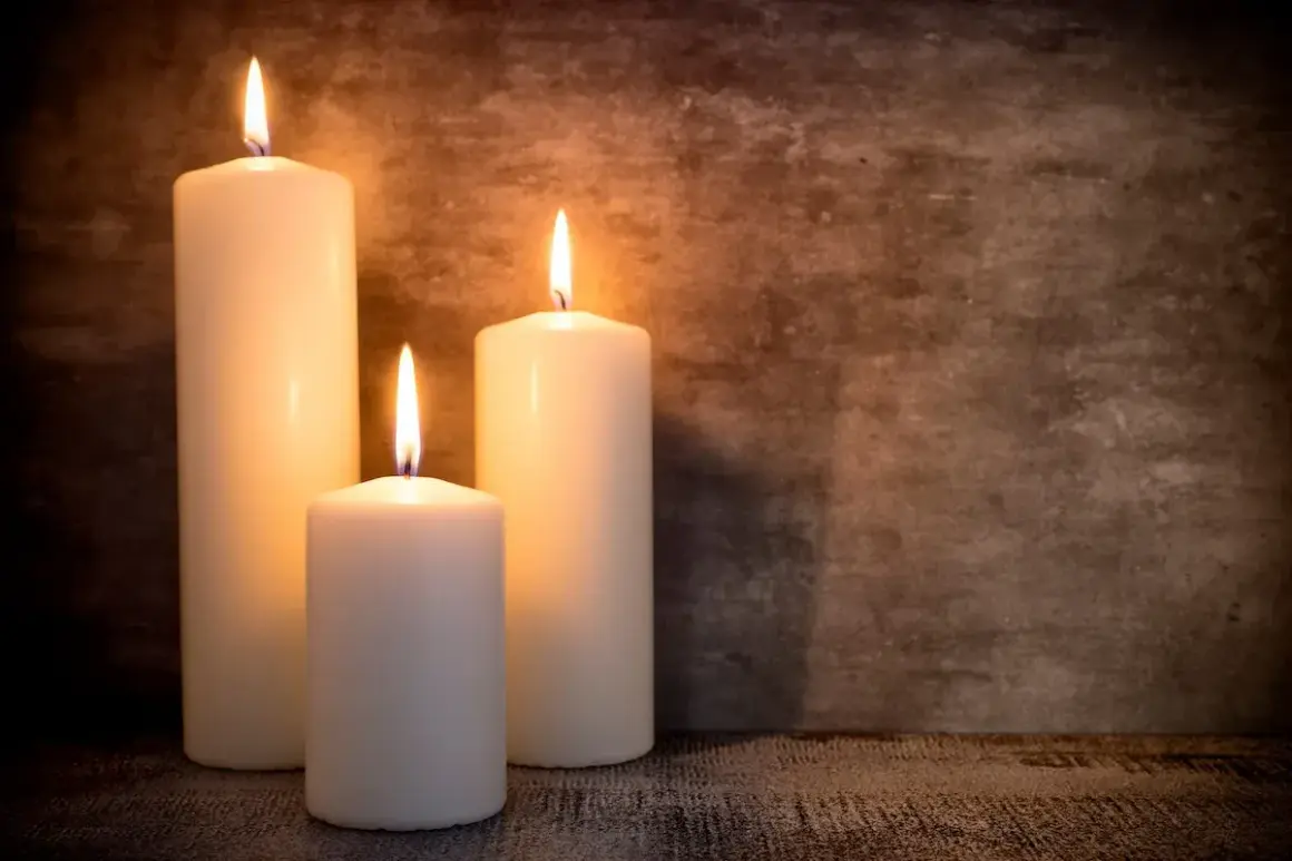 Tre candele di cera bianca illuminate, con fiamme danzanti, su uno sfondo scuro. Un'atmosfera intima, perfetta per riflettere su dove si buttano le candele di cera.