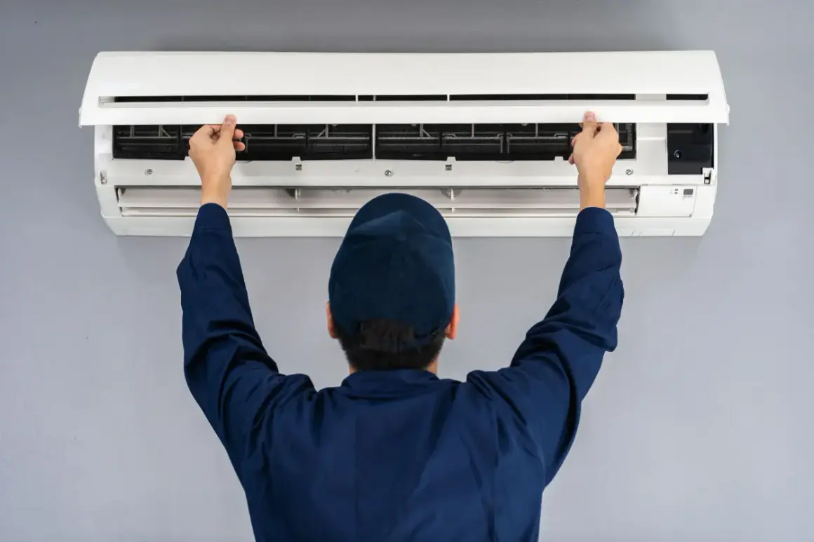 Tecnico apre il pannello di un condizionatore split per manutenzione. Il riscaldamento con split è efficiente.