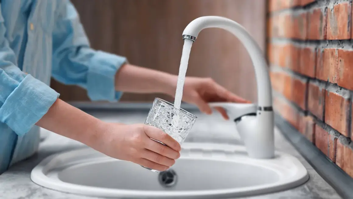 Mani che riempiono un bicchiere d'acqua dal rubinetto. L'acqua sanitaria cos'è? È l'acqua potabile che arriva nelle nostre case.