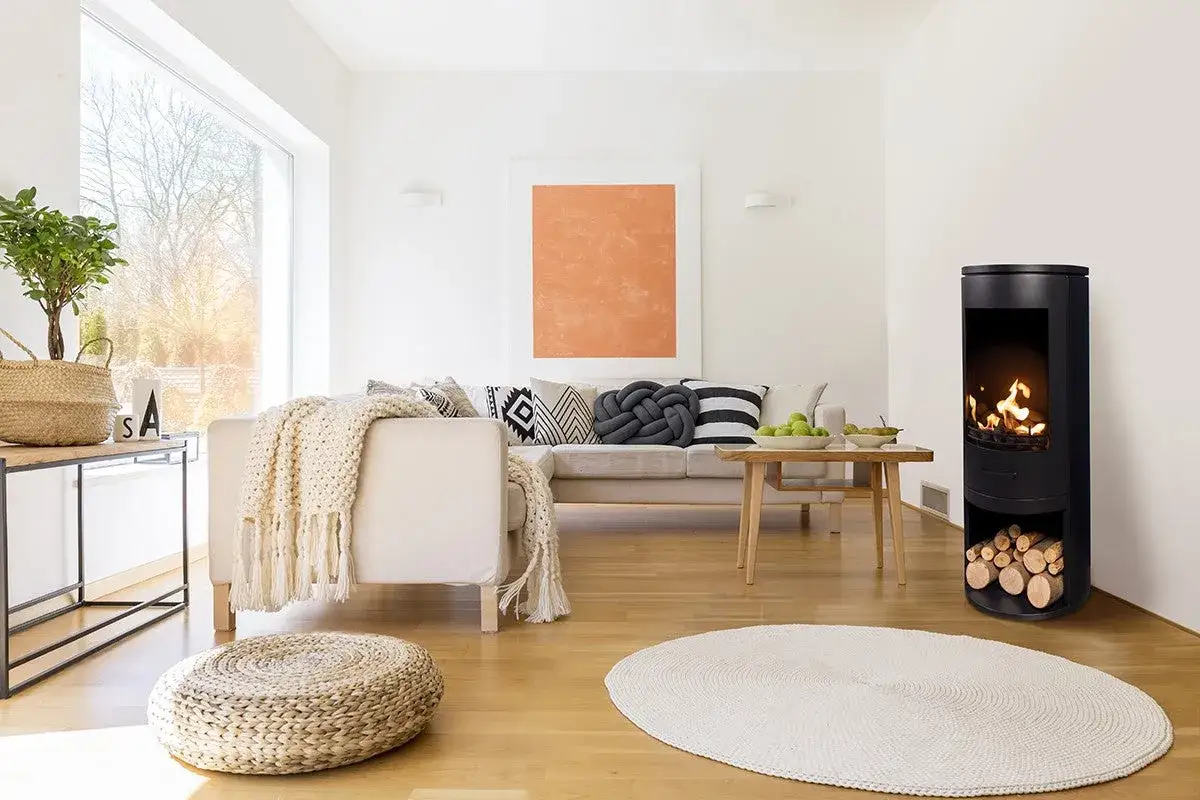 Salotto moderno con stufa a bioetanolo accesa, divano beige, cuscini decorativi e un grande quadro arancione. Conviene la stufa a bioetanolo per un ambiente caldo e accogliente.