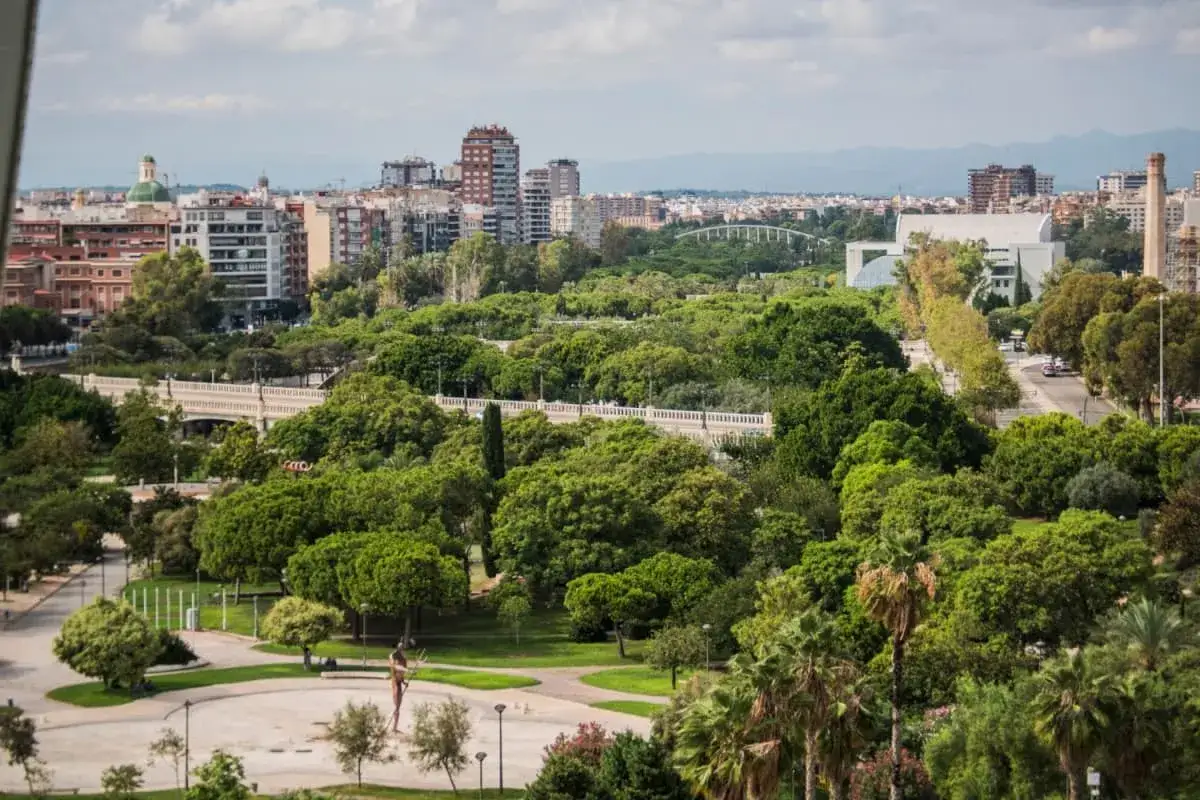 Un paesaggio urbano verdeggiante con edifici sullo sfondo, un parco rigoglioso e un ponte, che incarna il goal 11 agenda 2030 per citt&agrave; sostenibili.