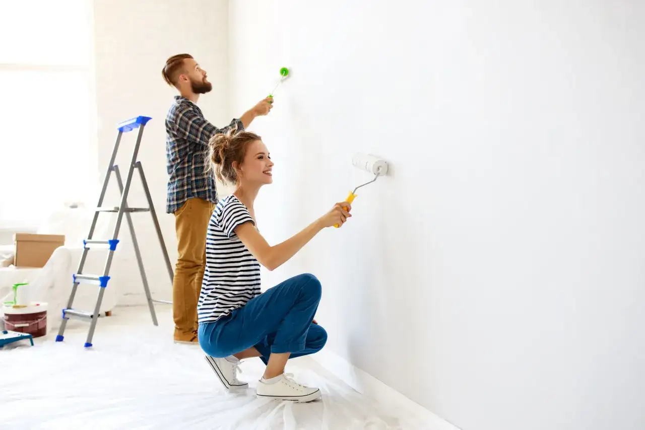 Coppia felice applica nuove tecniche di pittura pareti con rulli, rinnovando la casa con gioia.