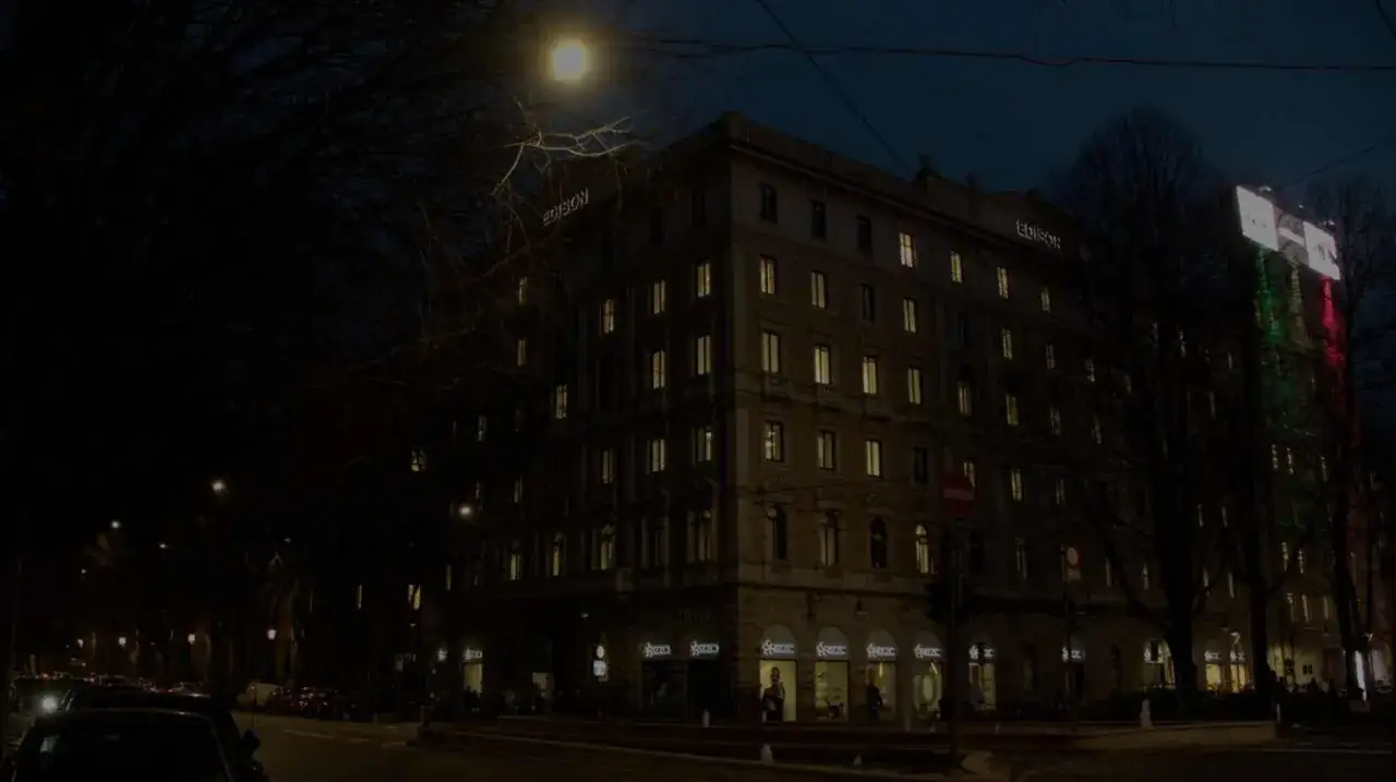 Edificio illuminato di notte, con insegne luminose e un grande schermo che proietta i colori della bandiera italiana. Un'atmosfera suggestiva per il 16 febbraio, giornata mondiale.