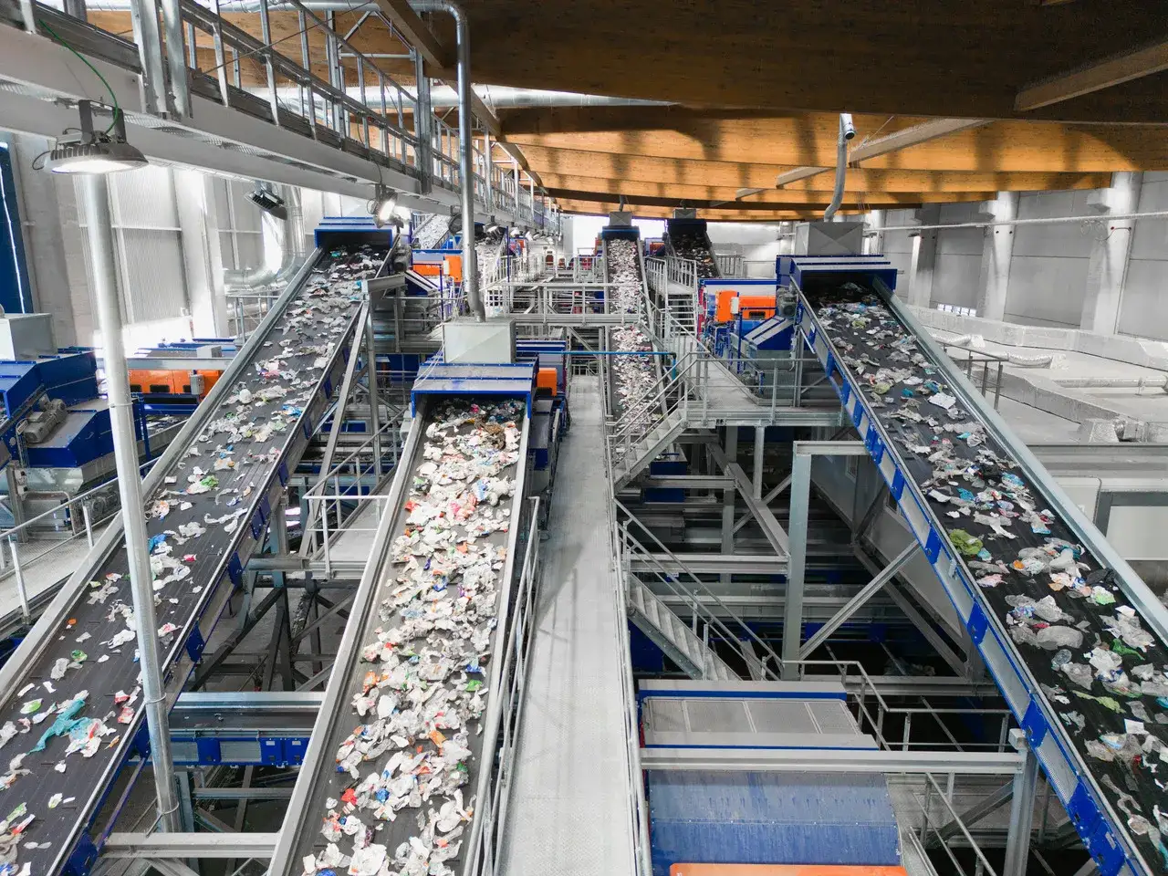Impianto di selezione rifiuti con nastri trasportatori carichi di materiali destinati a diventare materie prime seconde.