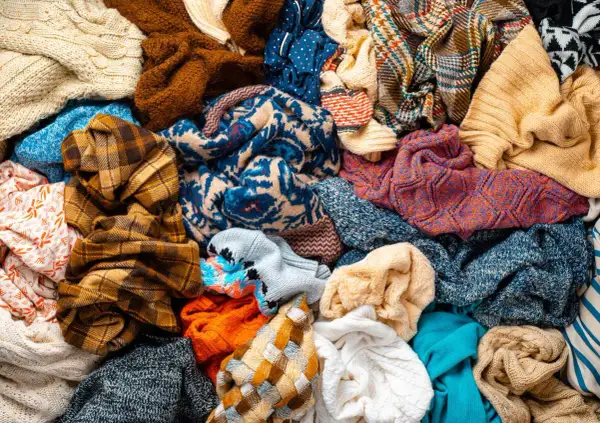 Un mucchio di vestiti colorati, pronti per la raccolta indumenti usati. Maglioni, sciarpe e tessuti di varie fantasie e trame.